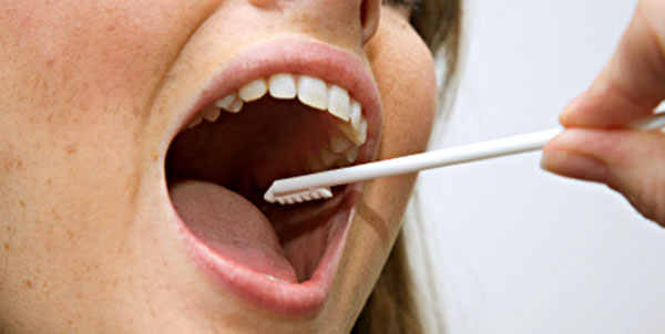 A woman is having the inside of her cheek swabbed with a collection brush.